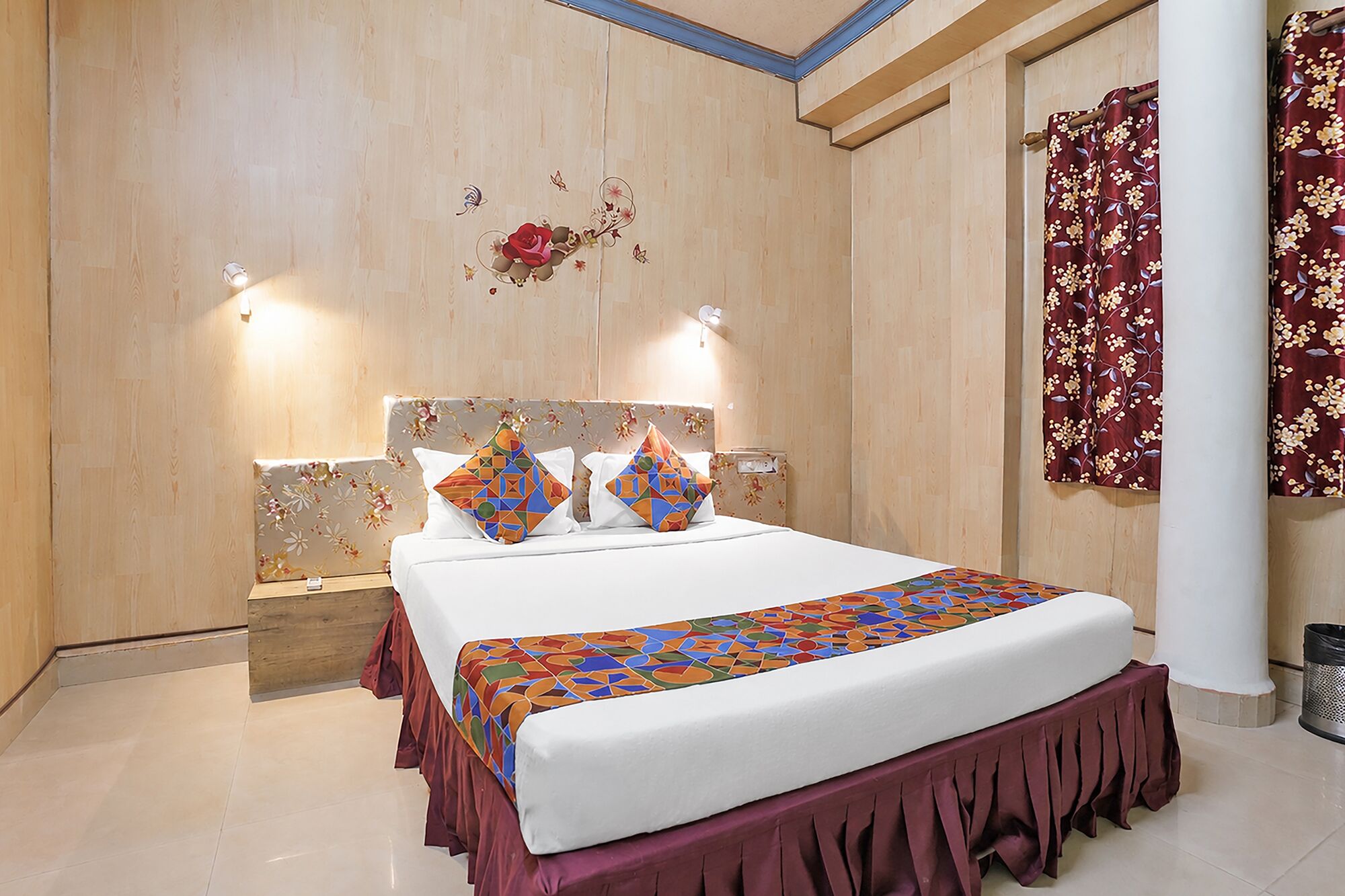 Habitación de hotel con una cama grande, cabecera de madera, pared decorativa y cortina con estampado floral.