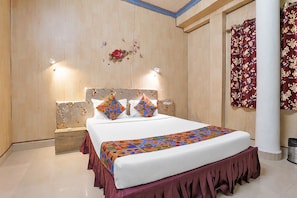 A hotel room with a large bed, a wooden headboard, a decorative wall, and a curtain with a floral pattern. - FabHotel Manvin's Inn (Panaji)