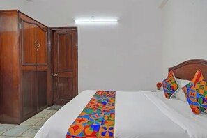A hotel room with a bed, a wooden wardrobe, and a colorful bed runner.
