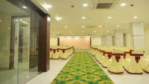 A hotel conference room with rows of chairs, a patterned carpet, and a glass partition on one side. - Fabhotel Swagath Grand (Khammam)