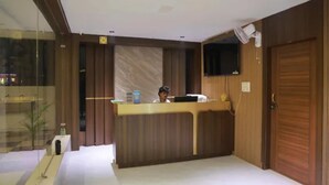 A reception area with a wooden counter, a television mounted on the wall, and a closed wooden door. - Fabhotel Swagath Grand (Khammam)