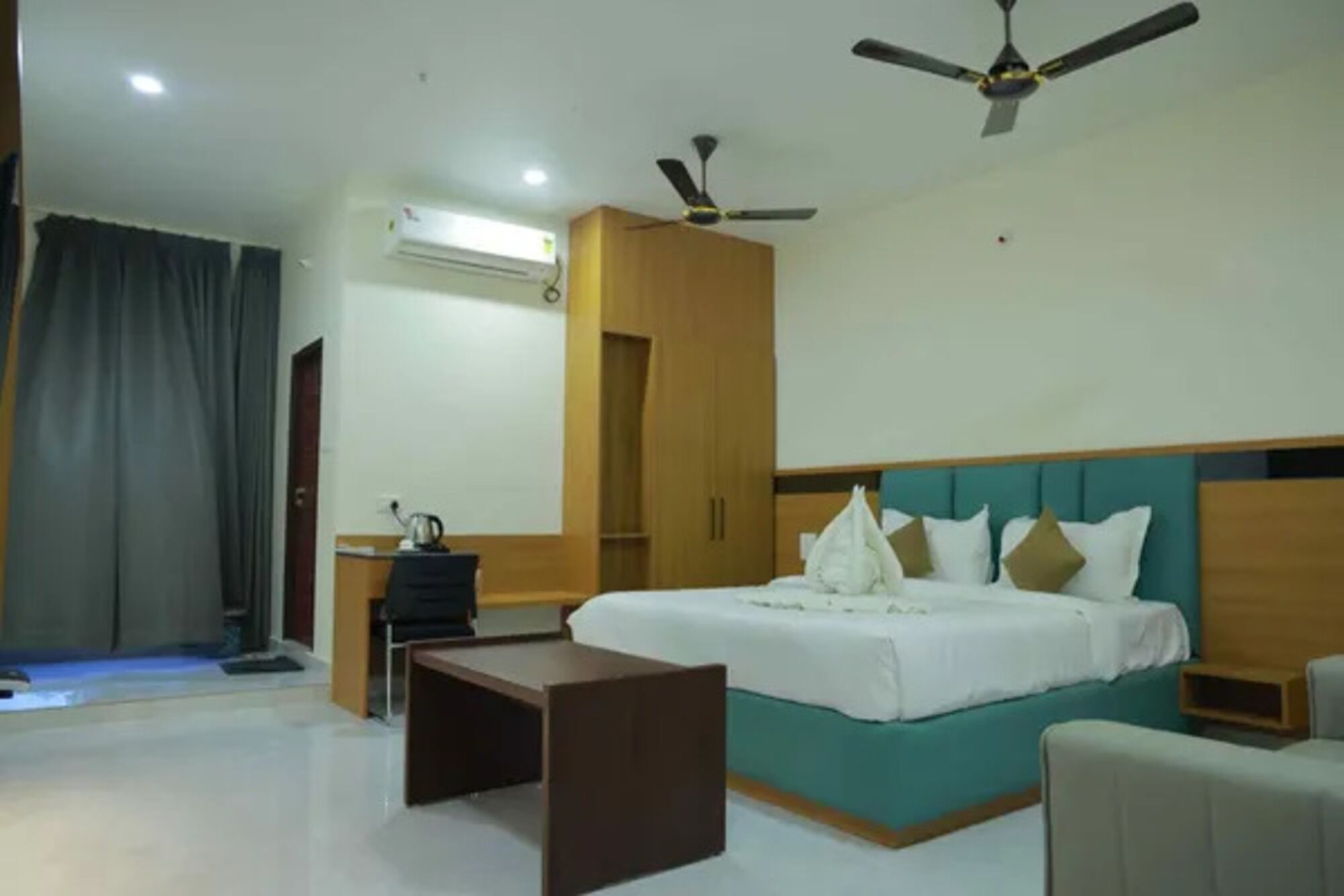 Een hotelkamer met een bed, een bureau, een stoel, een plafondventilator en een airconditioning.