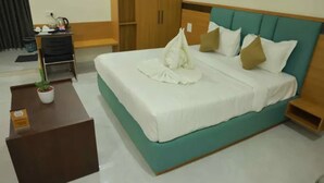 A neatly made bed with white linens and a teal headboard, a small wooden table with a potted plant, and a wooden wardrobe in a hotel room. - Fabhotel Swagath Grand (Khammam)