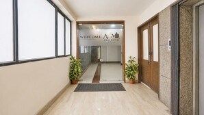 En hotellentrén med en receptionsdisk, en skylt med texten ”Välkommen” och krukväxter.
