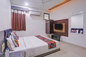A hotel room with a bed, a TV, a wardrobe, and an air conditioning unit. - FabHotel Agm (Ahmedabad)