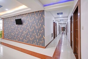 Ein moderner Hotelkorridor mit Wandmuster, einem Flachbildfernseher und einer langen Diele zu mehreren Türen.