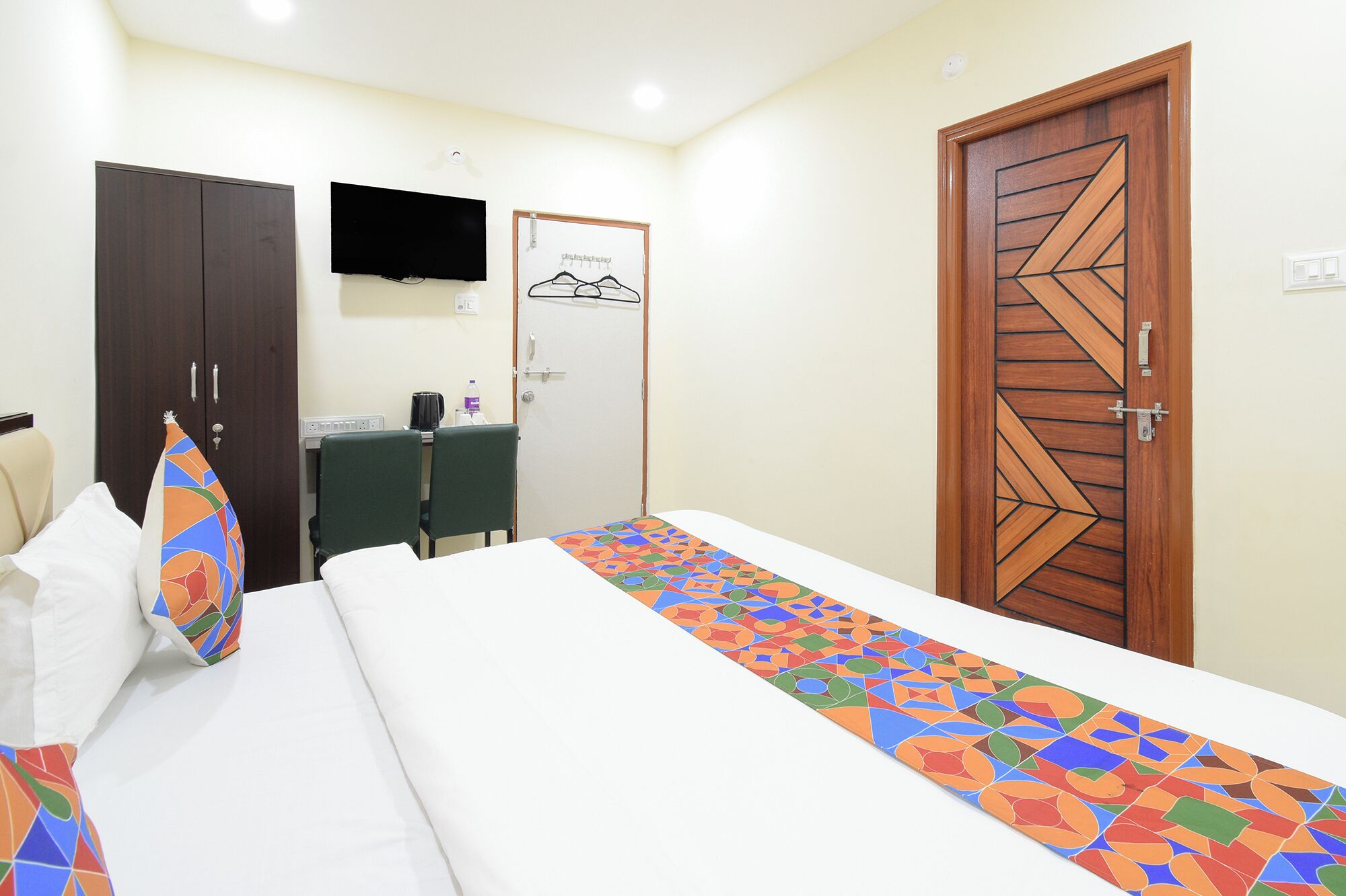 A hotel room with a bed, a desk, a chair, a TV, and a wardrobe.