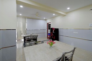 Un salón de conferencias con una mesa de mármol, sillas, una pizarra, un ventilador de techo y un refrigerador.