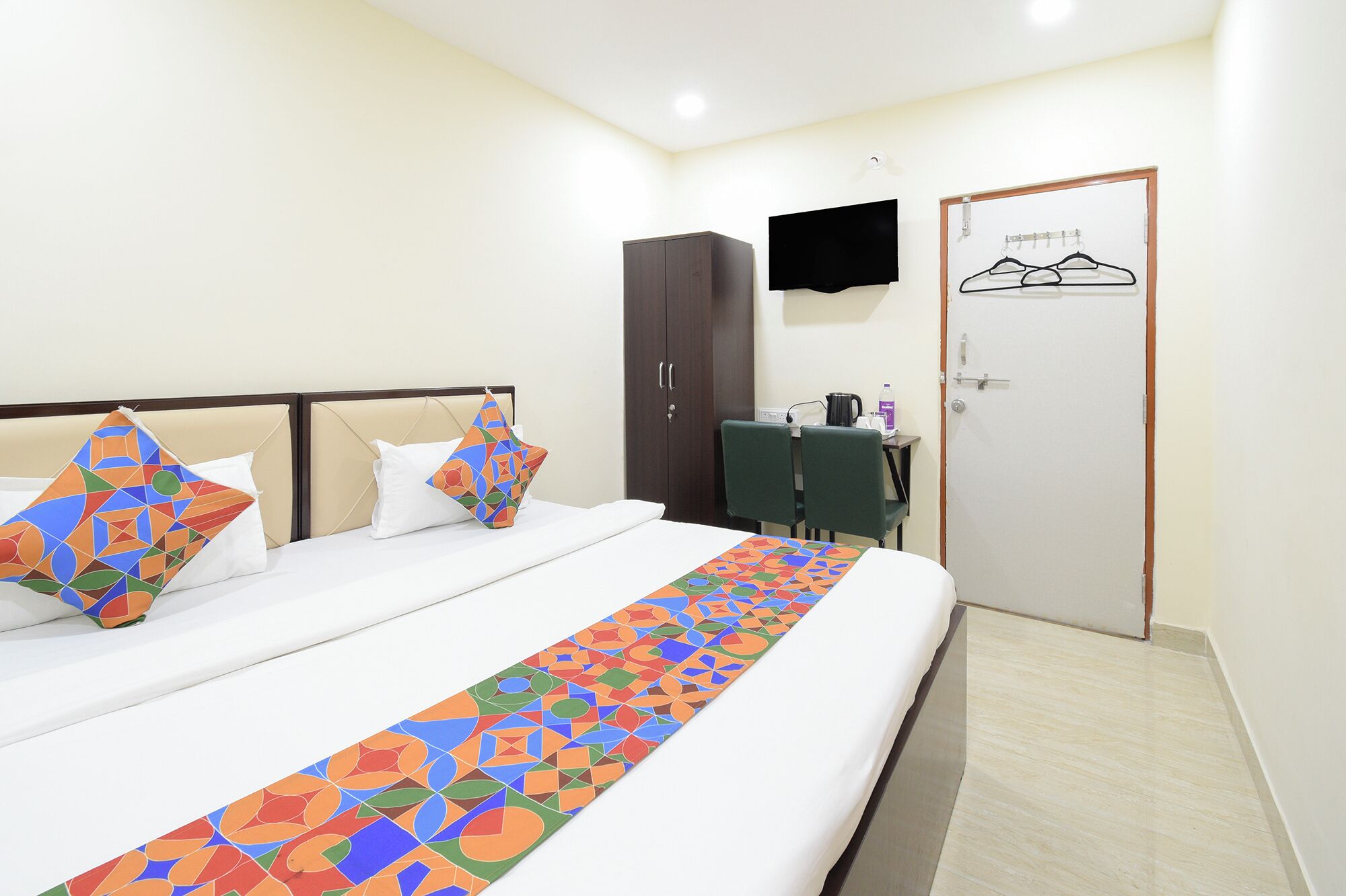 Quarto de hotel com uma cama, uma escrivaninha, um guarda-roupa e uma televisão.