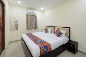 Habitación de hotel con cama, mesita de noche, aire acondicionado, espejo y ventana con cortinas.