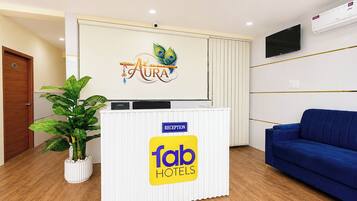 A reception desk with a logo, a reception sign, a TV, and a blue sofa.