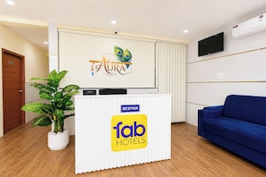 A reception desk with a logo, a reception sign, a TV, and a blue sofa. - Fabhotel Swagath Inn (Hyderabad)
