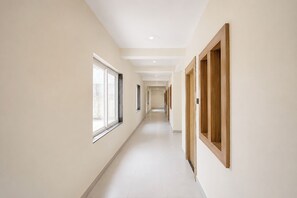 A corridor with a window on the left and a wooden door on the right. - Fabhotel Ramanjnaeya (Faizabad)