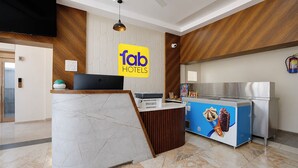 Zona de recepción de hotel con diseño moderno, que incluye un mostrador de mármol, una pantalla digital y un mostrador azul con imágenes de helados.