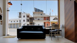 Un interior moderno con un sofá negro, una mesa de comedor con sillas y vistas a edificios urbanos.