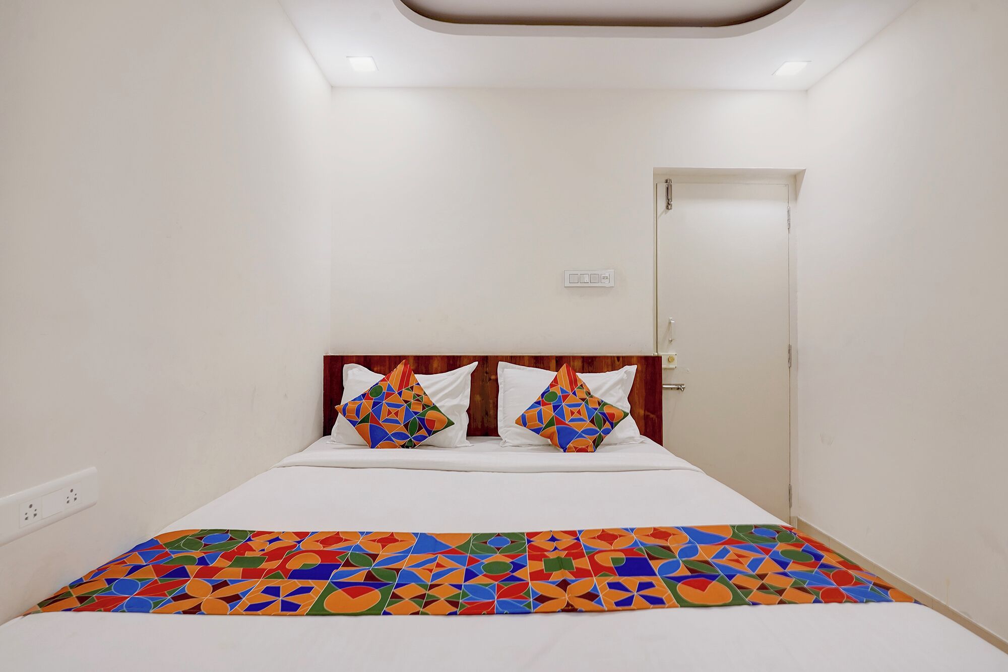 Una cama individual con una colcha de diseño geométrico y colorido, y dos almohadas con un diseño similar.