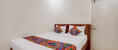 A single bed with a colorful geometric-patterned bedspread, a wooden headboard, and two decorative pillows.