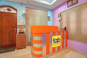En receptionsdisk med et skilt der siger 'fab hotels', en trædør og et vindue med persienner.