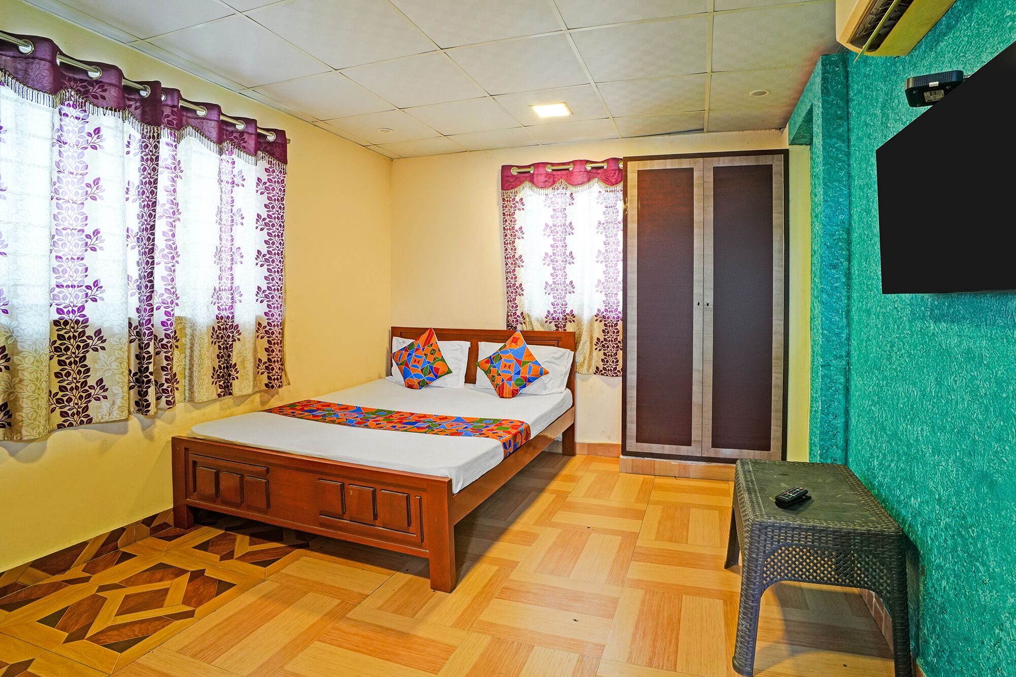 Un dormitorio con cama de madera, cortinas estampadas, un armario y una pequeña mesa.