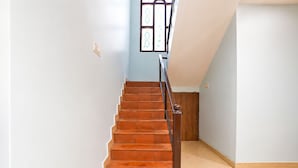 Eine Treppe mit Holzboden und Metallgeländer, die zu einer Zwischenebene mit einer hellblauen Wand und einem Fenster mit verzierten Glasscheiben führt.