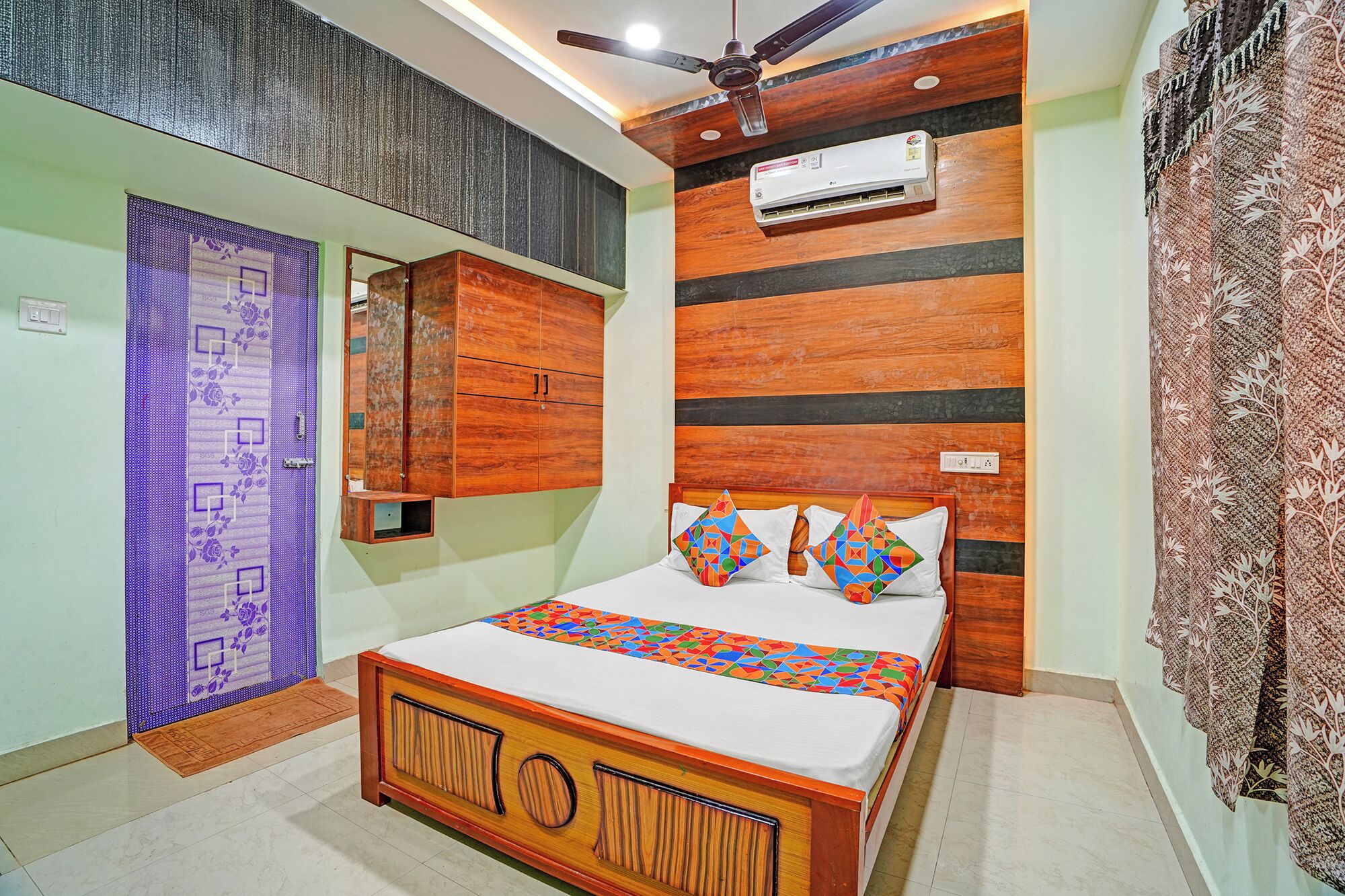 Un dormitorio con cama, ventilador de techo, equipo de aire acondicionado, espejo y cortina estampada.