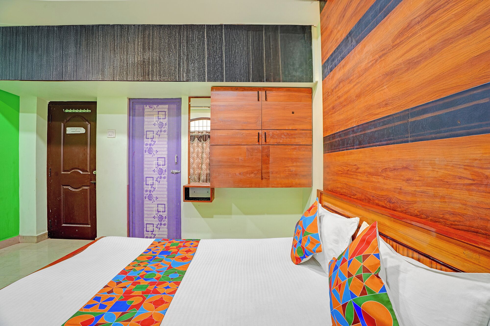 Una habitación de hotel con una cama, un cabecero de madera, una puerta con un letrero y una pared con textura.