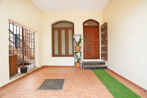 A hallway with a tiled floor, a metal gate, a wooden door with glass panels, and a potted plant. - FabHotel Heavens Inn (Chennai)