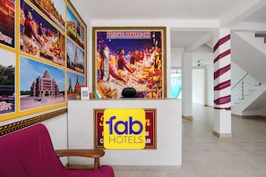 Et hotelreceptionsområde med en stor plakat af en mand i traditionelt tøj, et skilt med 'fab hotels' og et indrammet fotografi af et tempel.