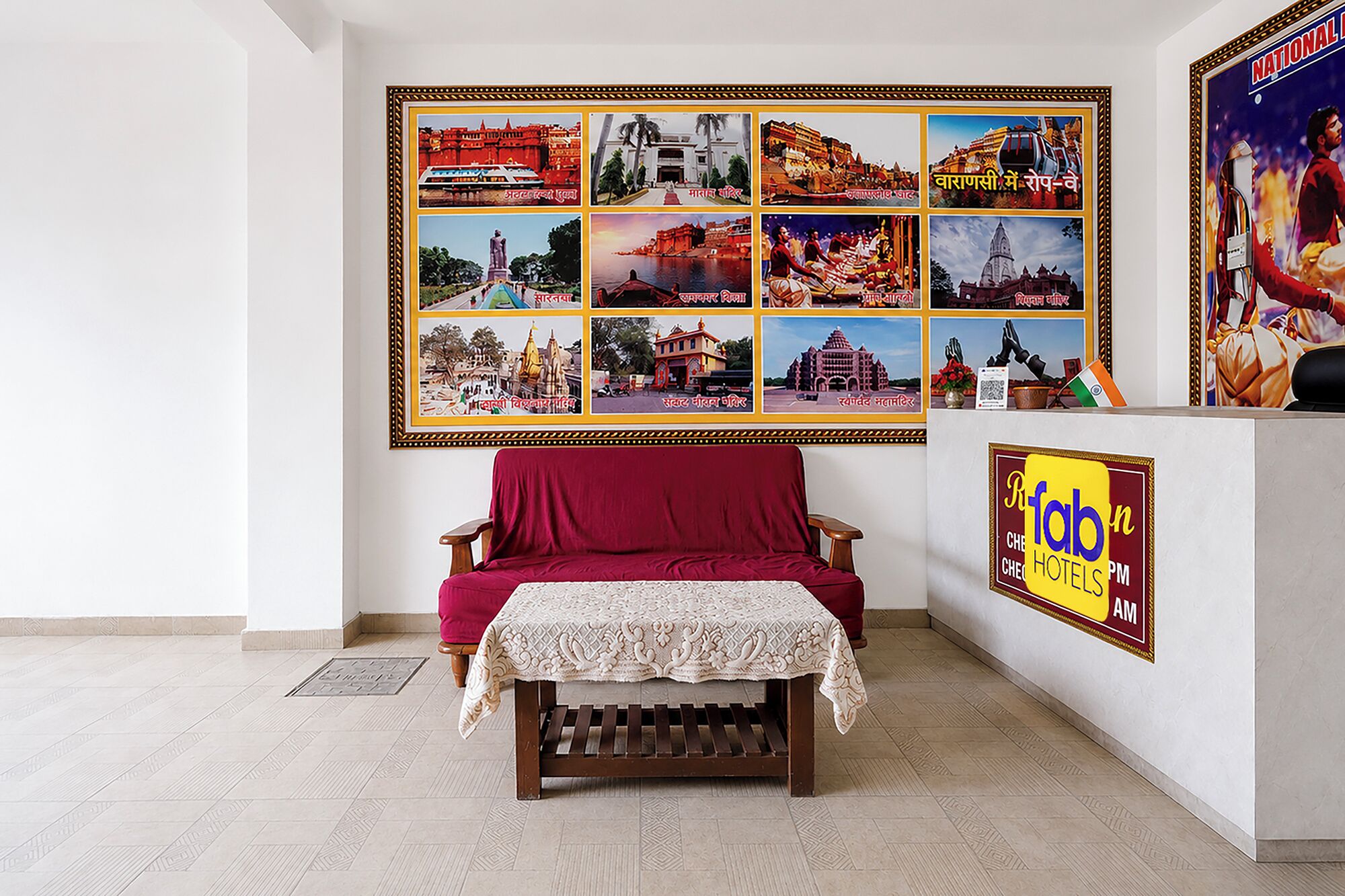 Zona de recepción de un hotel con un sofá rojo, una pequeña mesa con mantel de encaje y una pared decorada con un collage de fotografías del hotel.