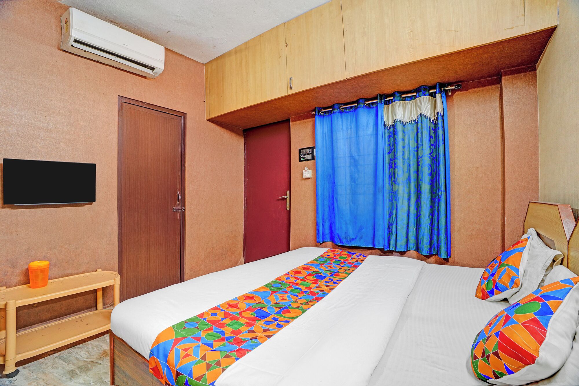 Une chambre à coucher comprenant un lit, une table de chevet, une armoire, une fenêtre avec des rideaux et un appareil de climatisation.