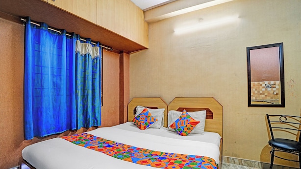Ein Hotelzimmer mit einem Bett, einem Sessel, einem Fenster mit Vorhängen und einem an der Wand befestigten Spiegel.
