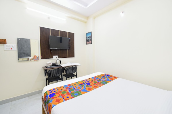 Habitación de hotel con cama, escritorio con silla, televisor montado en la pared y un pequeño marco de fotos.