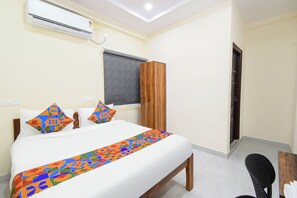 Habitación de hotel con cama, ventana con reja de metal, unidad de aire acondicionado y armario de madera.
