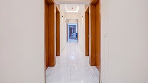 A corridor with wooden doors and a tiled floor, leading to a room with a bed and a window. - Fabhotel Royal Midway (Gandhinagar)