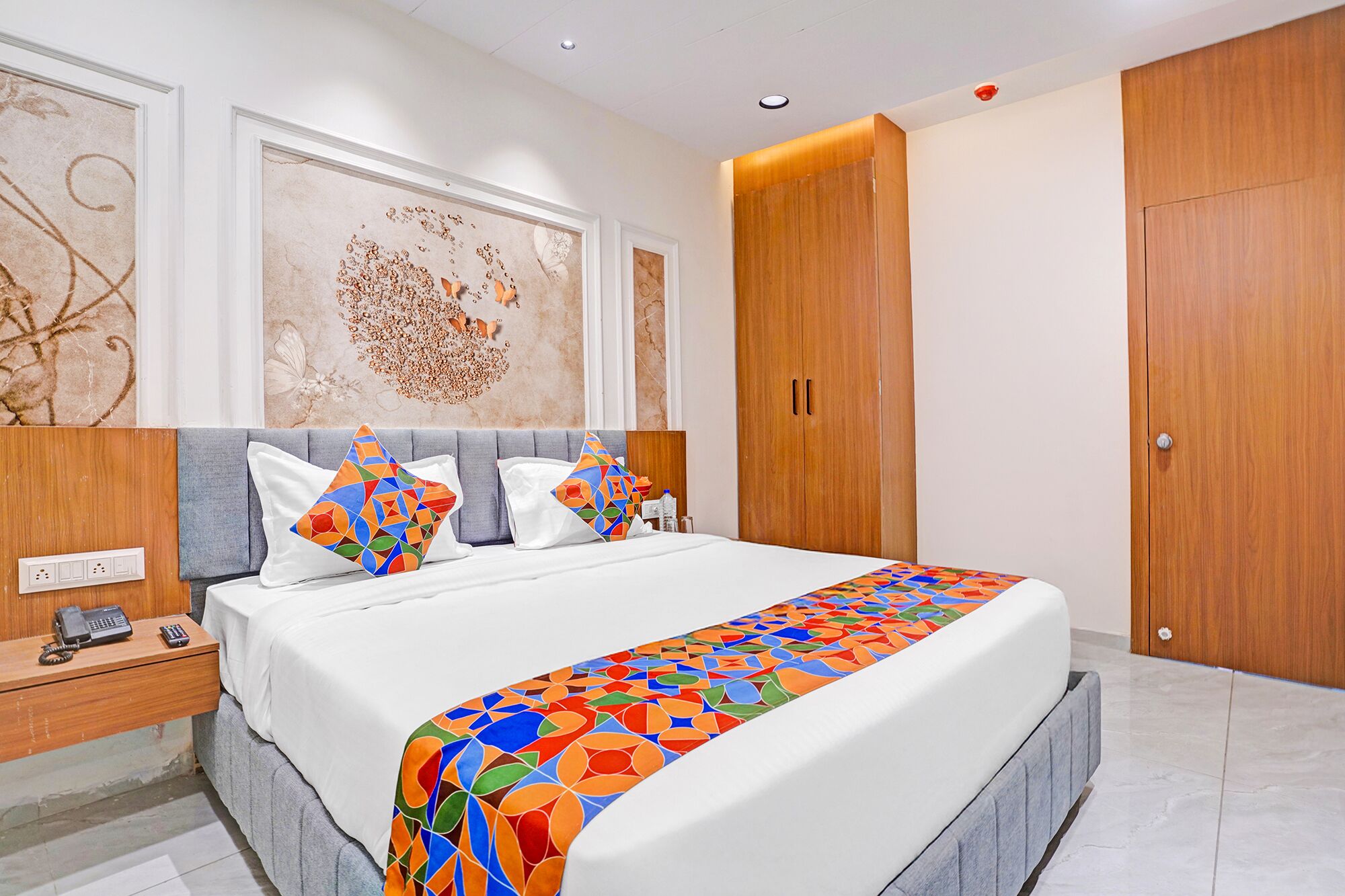 A modern bedroom with a large bed, a wooden wardrobe, and a nightstand with a telephone.