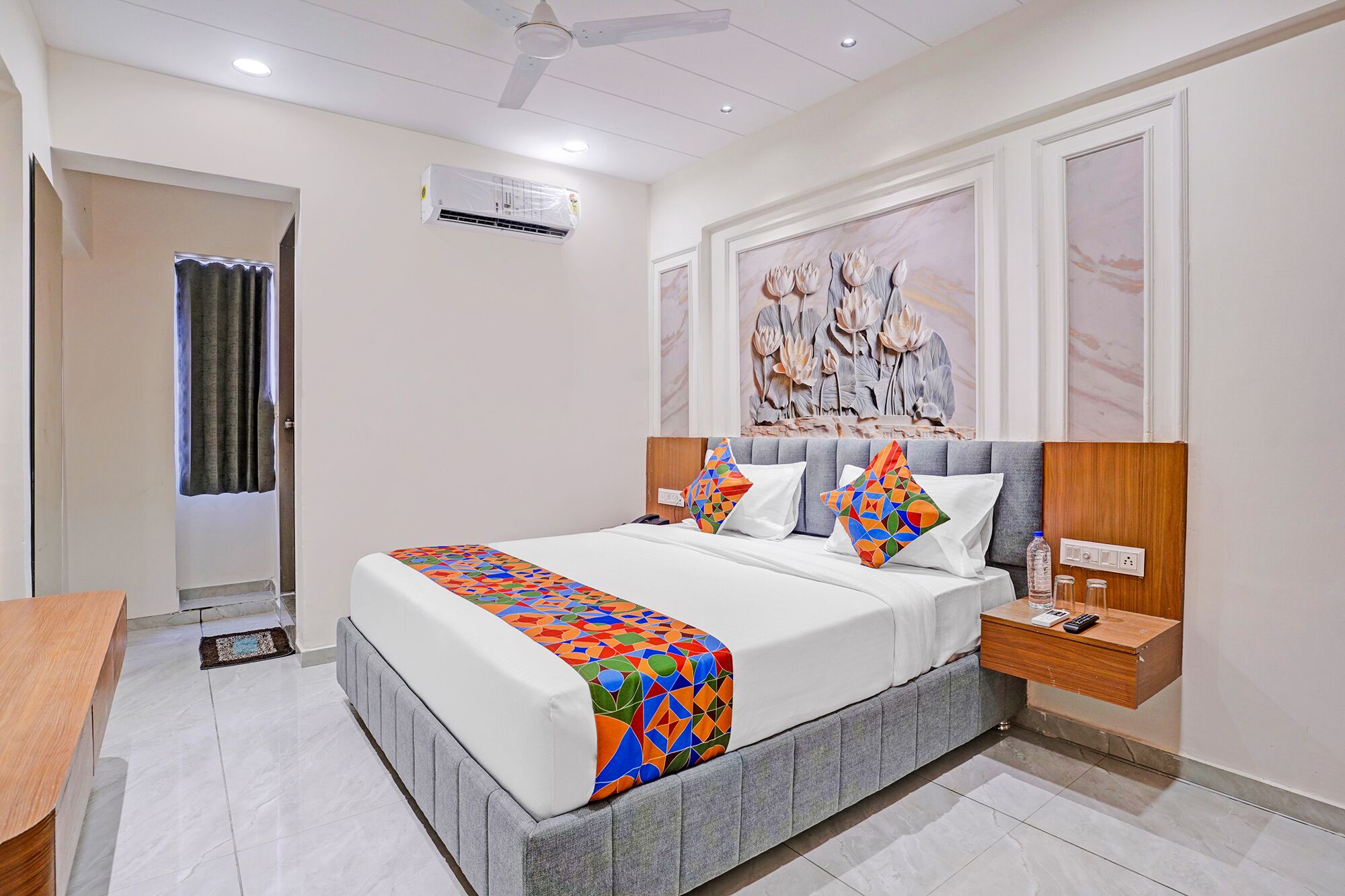 A hotel room with a bed, bedside table, and a wall-mounted air conditioner.