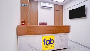A hotel reception desk with a check-in/out time sign, an air conditioning unit, a television, and a logo on the desk. - Fabhotel Royal Midway (Gandhinagar)