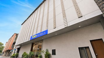 Un hotel con fachada moderna, un llamativo letrero azul y una serie de macetas con plantas en la entrada.