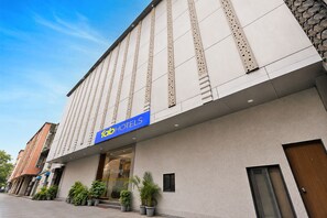 Un hôtel doté d’une façade moderne, d’une enseigne bleue bien visible et d’une série de plantes en pot disposées à l’entrée.