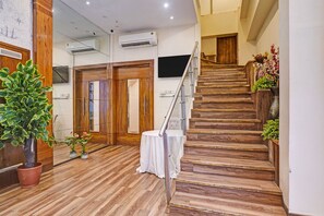 Un escalier en bois avec une rampe en métal, menant à une pièce où se trouvent une table et des chaises blanches.