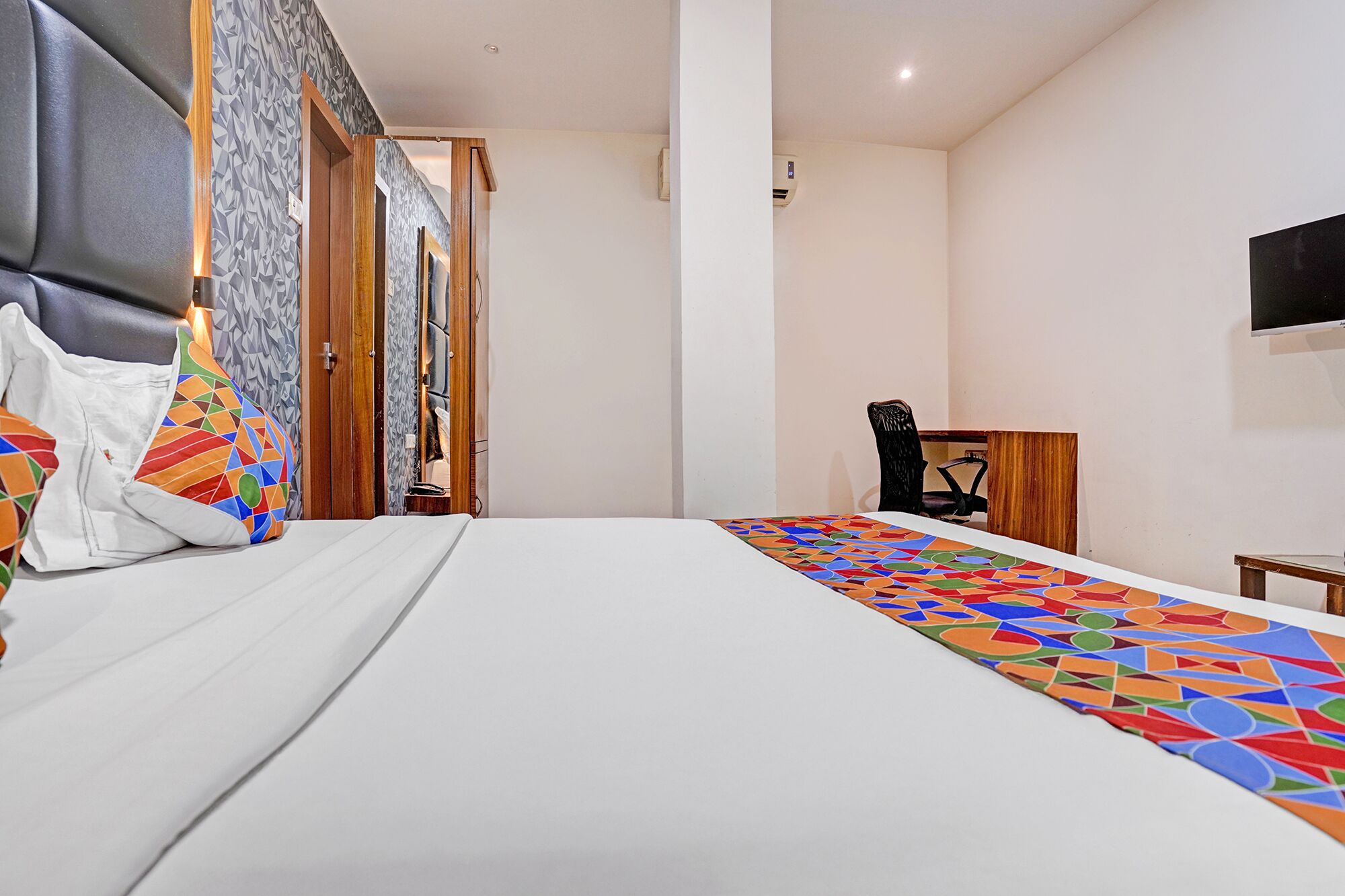 A hotel room with a bed, a desk, a chair, and a television on the wall.