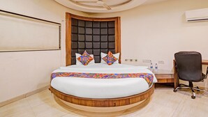 A bedroom with a round bed, a tufted headboard, a ceiling fan, a desk with a chair, and an air conditioning unit. - Fabhotel Address Inn (Mumbai)