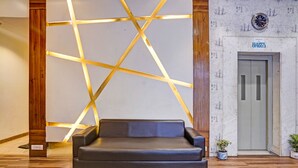 A modern lobby with a geometric light installation, a leather sofa, and a wall with a map and a clock. - Fabhotel Address Inn (Mumbai)