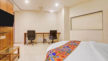 A hotel room with a bed, two office chairs, a desk, a television, and a ceiling fan.
