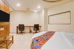 Quarto de hotel com uma cama, duas cadeiras de escritório, uma escrivaninha, uma televisão e um ventilador de teto.
