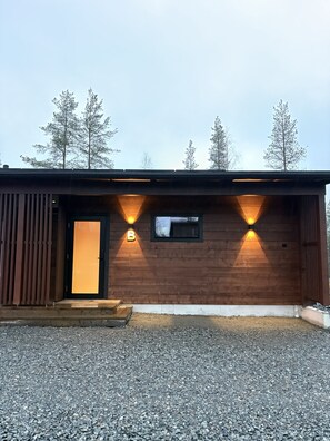 Un bâtiment en bois avec une porte noire et deux appliques murales illuminées.