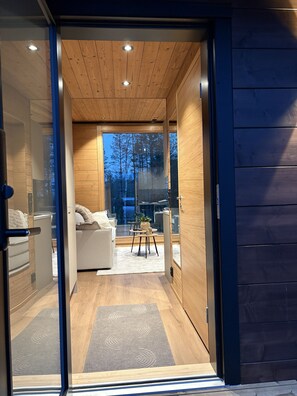 Un intérieur moderne avec un plafond en bois, un canapé blanc, une petite table et une vue sur les arbres à l’extérieur.