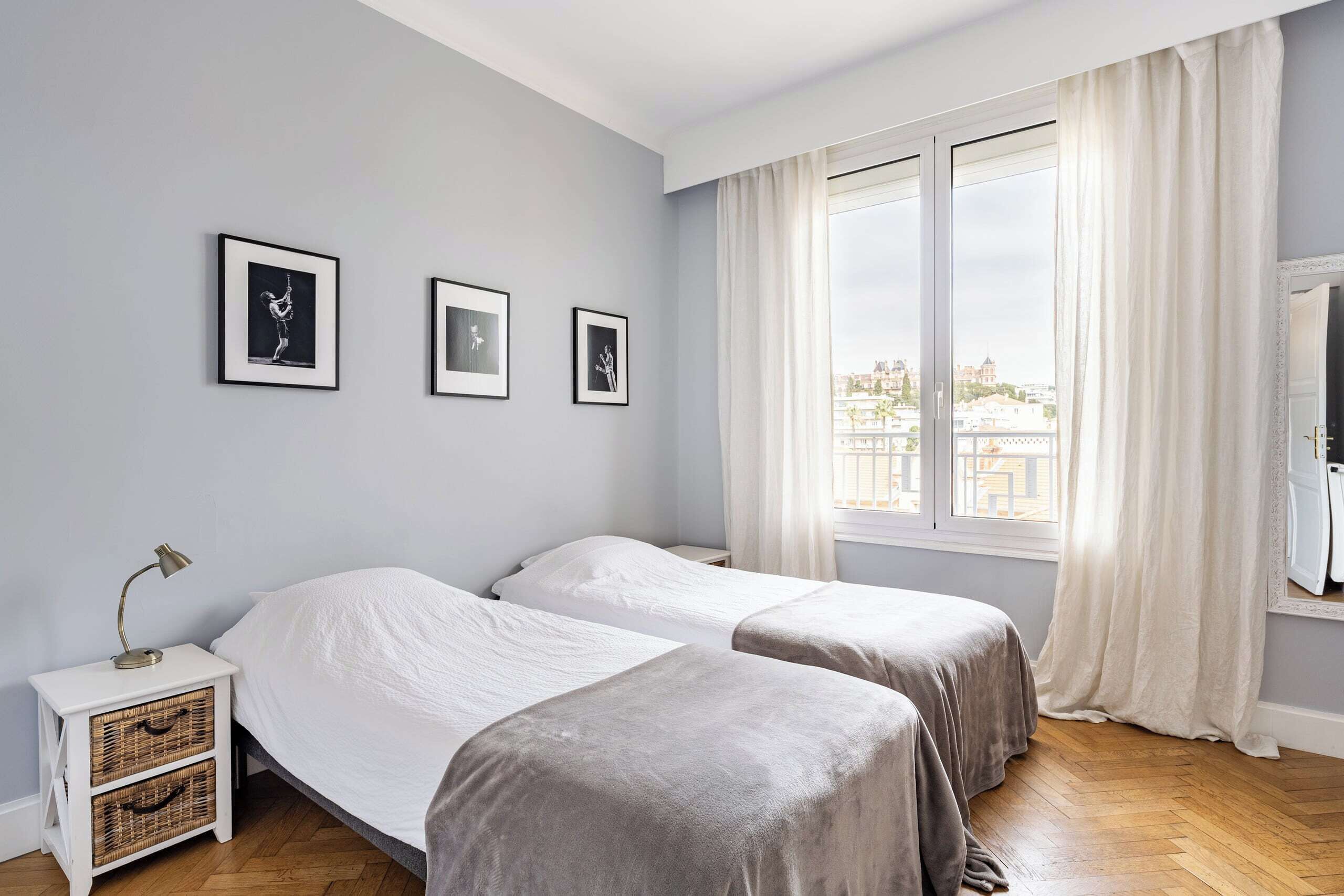 A bedroom with two beds, a nightstand, a lamp, and a window with curtains.