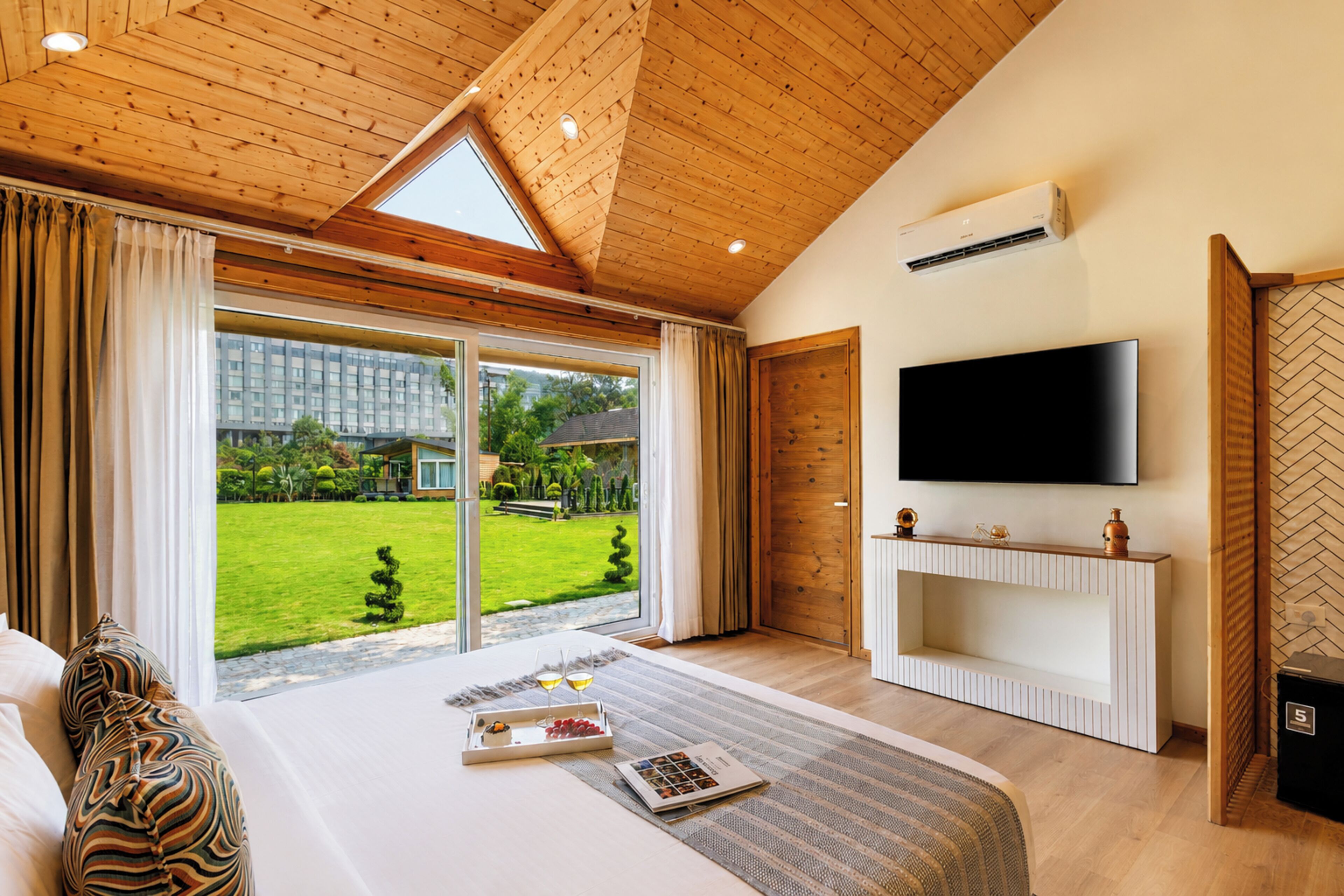 Ein Schlafzimmer mit einem großen Bett, einem an der Wand montierten Fernseher und einer Glastür, die in einen Garten führt.