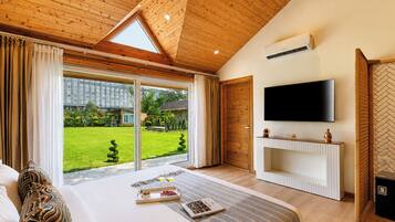 Ein Schlafzimmer mit einem großen Bett, einem an der Wand montierten Fernseher und einer Glastür, die in einen Garten führt.